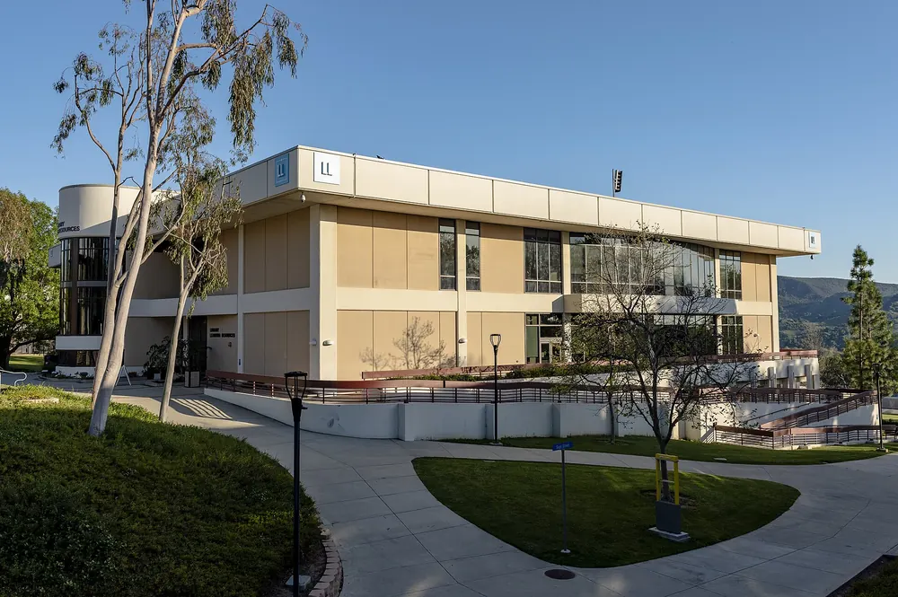 Modern two-story campus building with tall windows behind a curving lawn